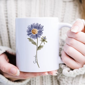 May include: White ceramic mug with a watercolor illustration of a purple flower and the name "Sarah" written in cursive.