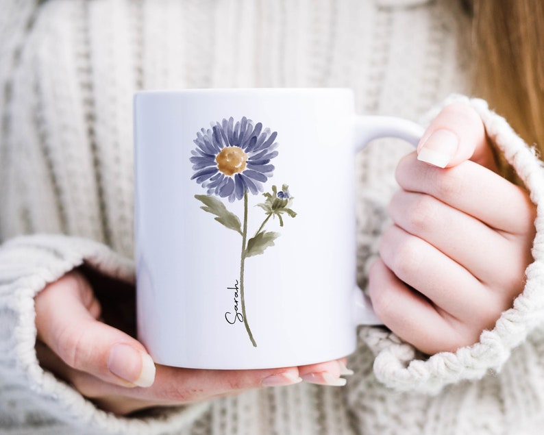 May include: White ceramic mug with a watercolor illustration of a purple flower and the name "Sarah" written in cursive.