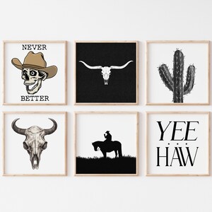 May include: Six black and white framed prints with western themes. The prints include a skull wearing a cowboy hat with the text "Never Better", a longhorn skull, a cactus, a silhouette of a cowboy riding a horse, and the text "Yee Haw".