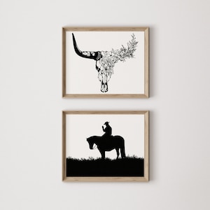 May include: Two framed black and white illustrations. The top illustration is a bull skull with flowers growing out of it. The bottom illustration is a silhouette of a person riding a horse.