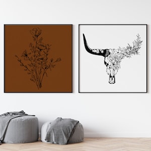 May include: Two black and white framed prints. The print on the left features a bouquet of flowers on a brown background. The print on the right features a bull skull with flowers on a white background.