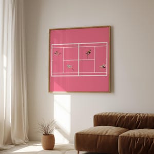 May include: A framed print of a pink tennis court with white lines and small figures of people playing tennis. The print is hanging on a white wall above a brown couch.