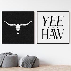 May include: Two black framed prints on a white wall. The print on the left features a white bull skull on a black background. The print on the right features the text "YEE HAW" in black on a white background.