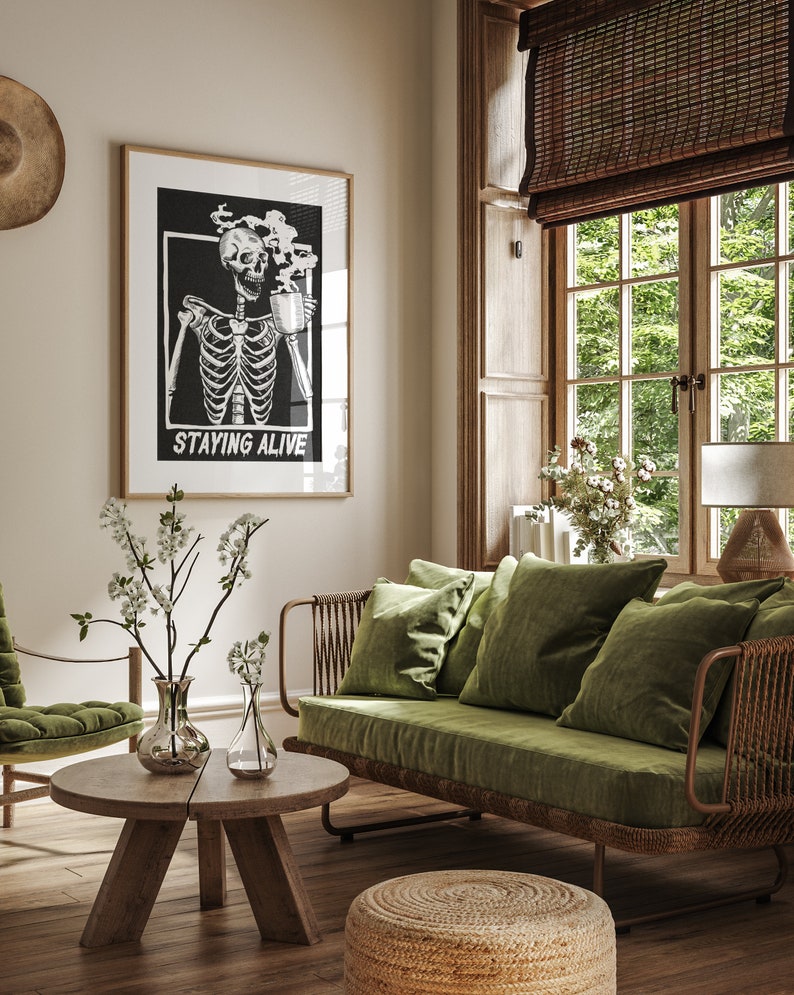 May include: A living room interior with a green velvet sofa, a wooden coffee table, and a framed black and white print of a skeleton drinking coffee with the text "Staying Alive".