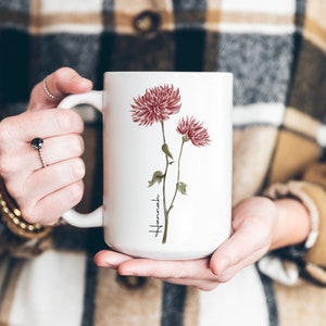 May include: White ceramic mug with a watercolor illustration of pink flowers and the word "Hamaki" in cursive.