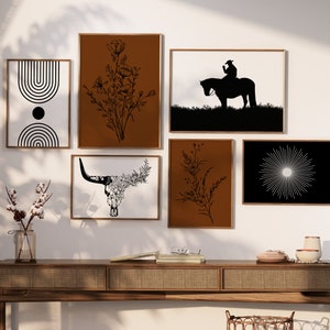May include: A set of eight black and white minimalist wall art prints with various designs, including a bull skull, a cowboy riding a horse, and a sunburst. The prints are framed in brown wood frames and are displayed on a wooden shelf.