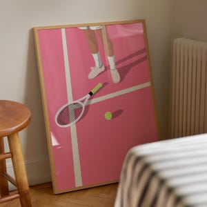May include: A framed illustration of a tennis player on a pink court. The player is wearing white sneakers and is holding a tennis racket. A tennis ball is on the court.