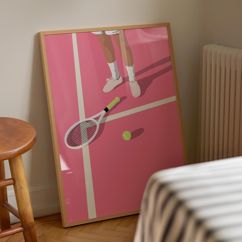May include: A framed illustration of a tennis player on a pink court. The player is wearing white sneakers and is holding a tennis racket. A tennis ball is on the court.