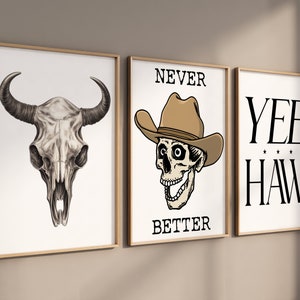 May include: Three framed prints with a western theme. The left print features a black and white drawing of a bull skull. The middle print features a skull wearing a cowboy hat with the text "NEVER BETTER". The right print features the text "YEE HAW" in black.