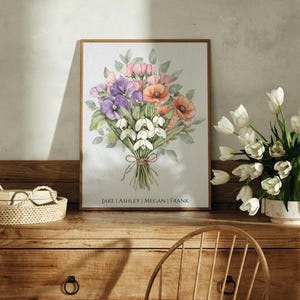 May include: A framed watercolor painting of a bouquet of flowers. The bouquet includes pink, white, and purple flowers. The names "Jake, Ashley, Megan, Frank" are printed at the bottom of the painting.
