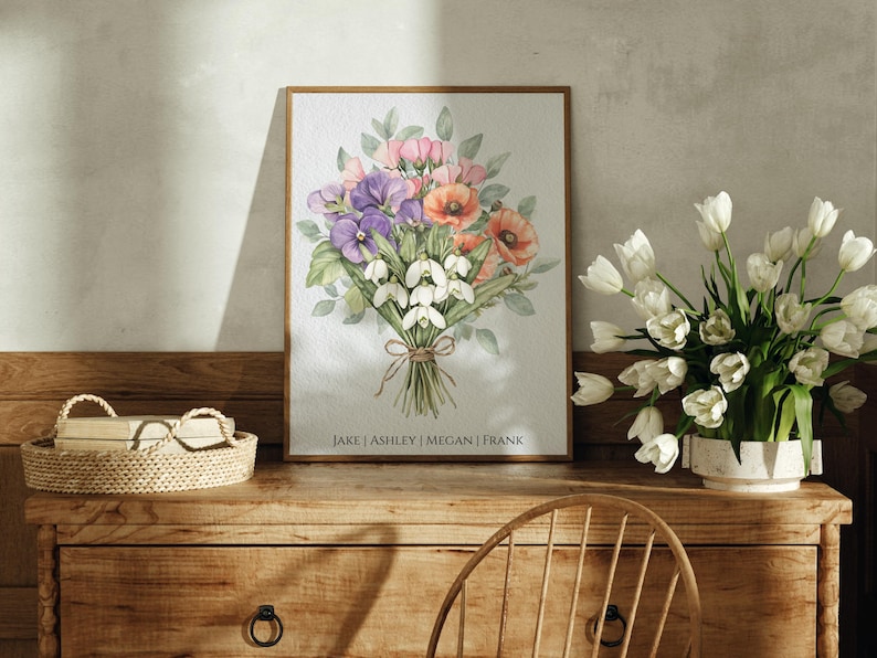 May include: A framed watercolor painting of a bouquet of flowers. The bouquet includes pink, white, and purple flowers. The names "Jake, Ashley, Megan, Frank" are printed at the bottom of the painting.