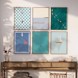 K&ouml;nnte beinhalten: Sechs gerahmte Drucke mit verschiedenen Sommerszenen, darunter ein kariertes Muster, ein Segelboot und Menschen, die im Meer schwimmen. Die Drucke h&auml;ngen an einer wei&szlig;en Wand &uuml;ber einem Holztisch.