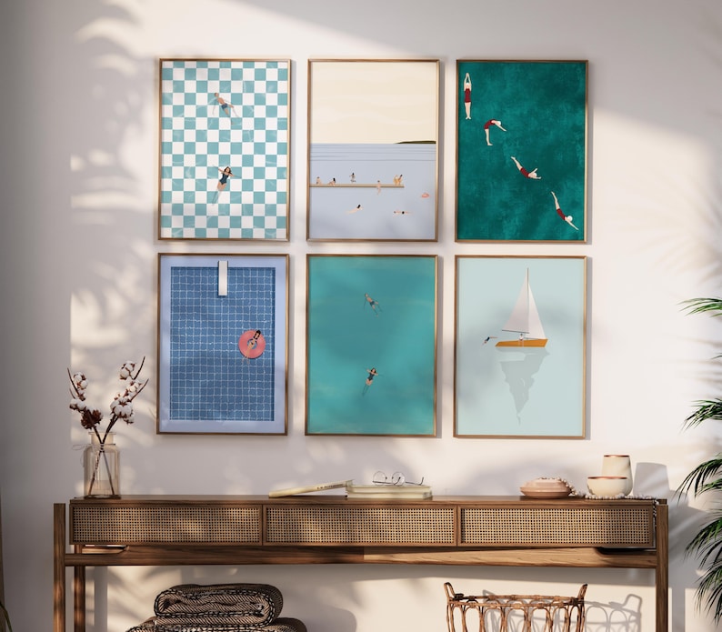 K&ouml;nnte beinhalten: Sechs gerahmte Drucke mit verschiedenen Sommerszenen, darunter ein kariertes Muster, ein Segelboot und Menschen, die im Meer schwimmen. Die Drucke h&auml;ngen an einer wei&szlig;en Wand &uuml;ber einem Holztisch.