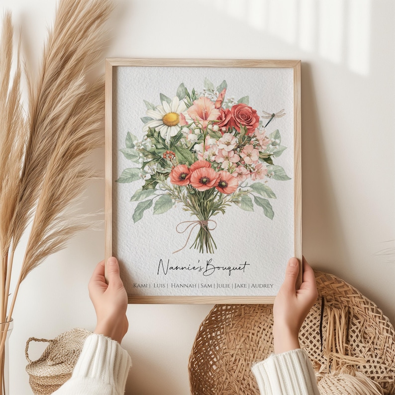 May include: A framed watercolor painting of a bouquet of flowers in shades of pink, red, and white. The bouquet is tied with a pink ribbon and the text 'Nannie's Bouquet' is written below the bouquet. The names 'Kami', 'Luis', 'Hannah', 'Sam', 'Julie', 'Jake', and 'Audrey' are listed below the text.