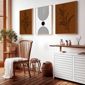 May include: A living room interior with a wooden chair, a side table, a white cabinet with a wooden top, and three framed prints on the wall. The prints feature black and white geometric designs and black and white floral illustrations on a brown background.