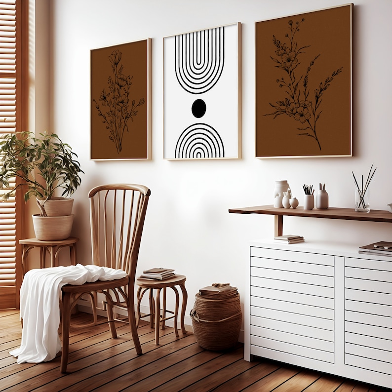 May include: A living room interior with a wooden chair, a side table, a white cabinet with a wooden top, and three framed prints on the wall. The prints feature black and white geometric designs and black and white floral illustrations on a brown background.