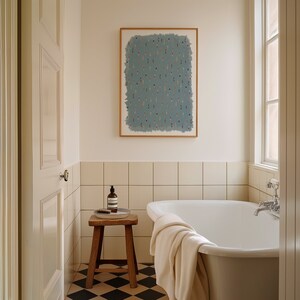 May include: A white bathtub with a white towel draped over the side. The bathtub is in a bathroom with white tile walls and a wooden stool with a bottle of soap on it. There is a framed picture on the wall above the bathtub.