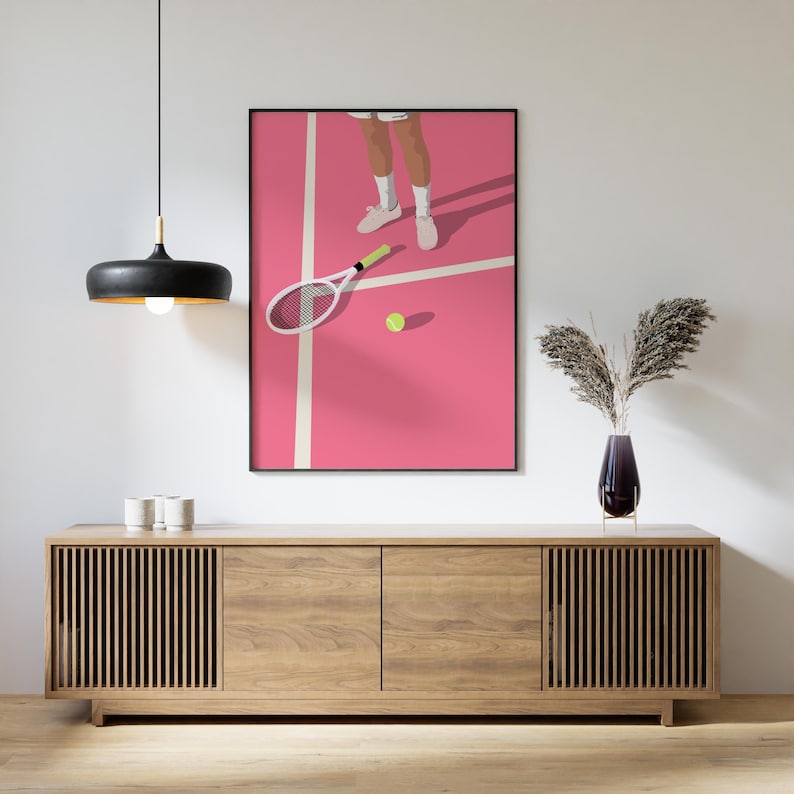 May include: A pink tennis court with a white line and a tennis racket lying on the court. A tennis ball is on the court. A person's legs and feet are visible in the background.