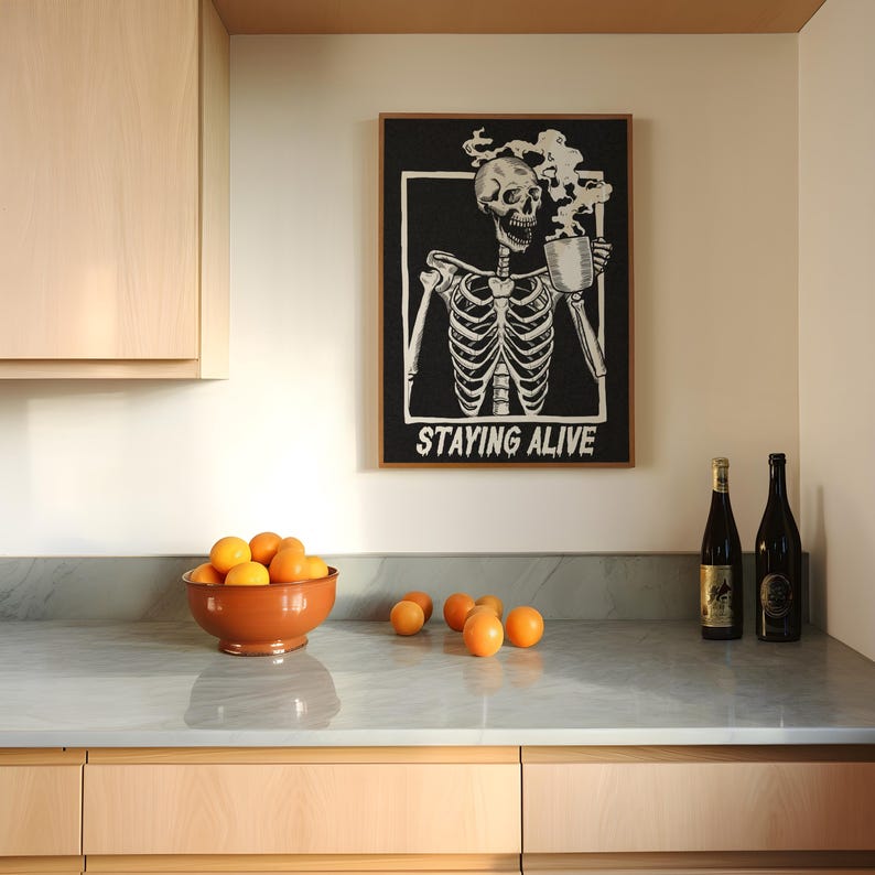 May include: A kitchen counter with a bowl of oranges, two bottles of wine, and a framed print of a skeleton drinking coffee with the text "Staying Alive".