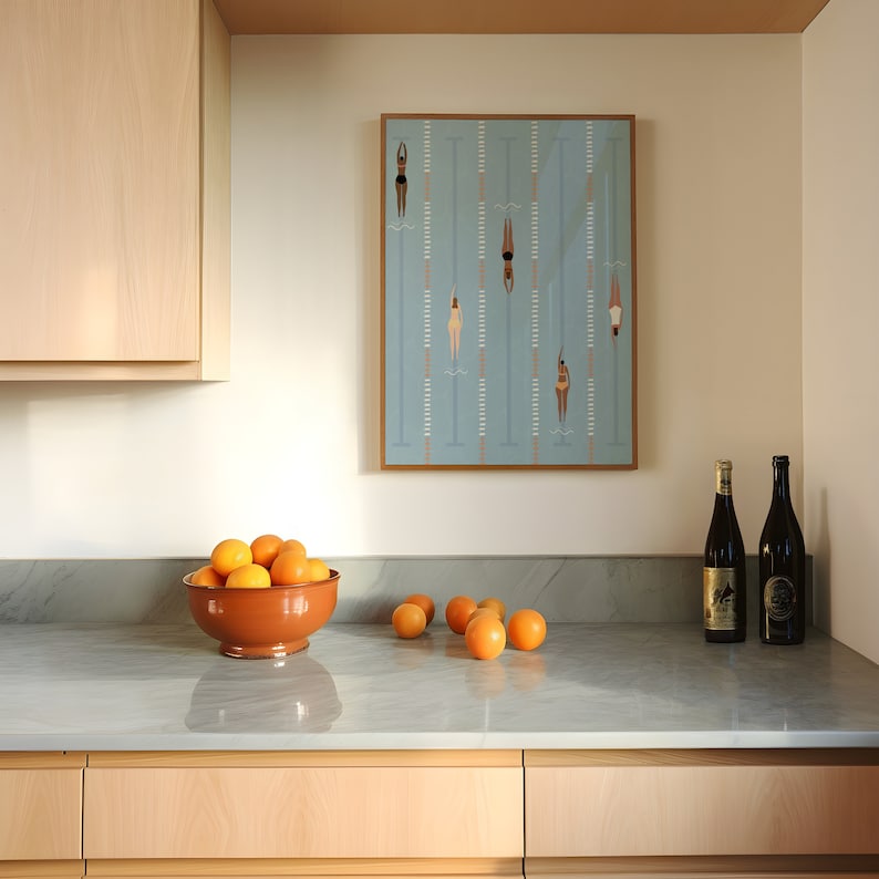May include: A kitchen counter with a bowl of oranges, two bottles of wine, and a framed print of swimmers in a pool.