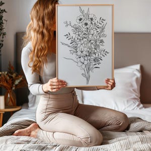 May include: A black and white line drawing of a bouquet of flowers in a simple wooden frame. The drawing features various types of flowers, including roses, lilies, and daisies.