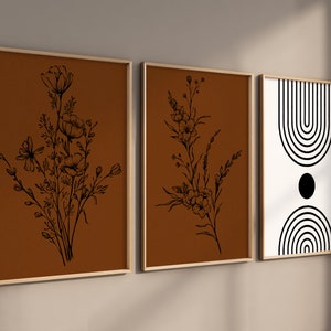 May include: Three framed prints with a minimalist aesthetic. The left and centre prints feature black line drawings of flowers on a brown background. The right print features a black and white geometric design with a circle and curved lines.