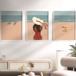 May include: Three framed illustrations of a beach scene. The leftmost illustration shows two people surfing. The middle illustration shows a woman in a red swimsuit and a large white sun hat. The rightmost illustration shows a beach umbrella and a beach chair.