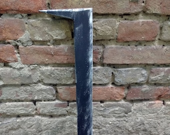 May include: A black, weathered, wooden sword with a slightly curved blade. The sword is leaning against a brick wall.