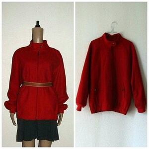 May include: A red wool bomber jacket with a zipper closure and a brown leather belt. The jacket has a stand-up collar and long sleeves.