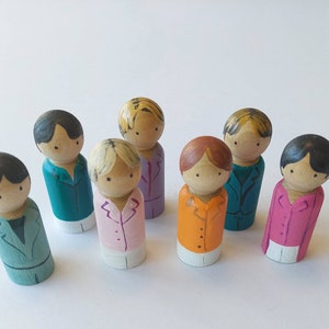 Può includere: Bambole di legno dipinte a mano in vari colori. Ogni bambola è dipinta con un abito o una camicia di colore diverso, tra cui verde acqua, rosa, arancione e viola. Le bambole hanno lineamenti semplici e capelli neri o biondi.