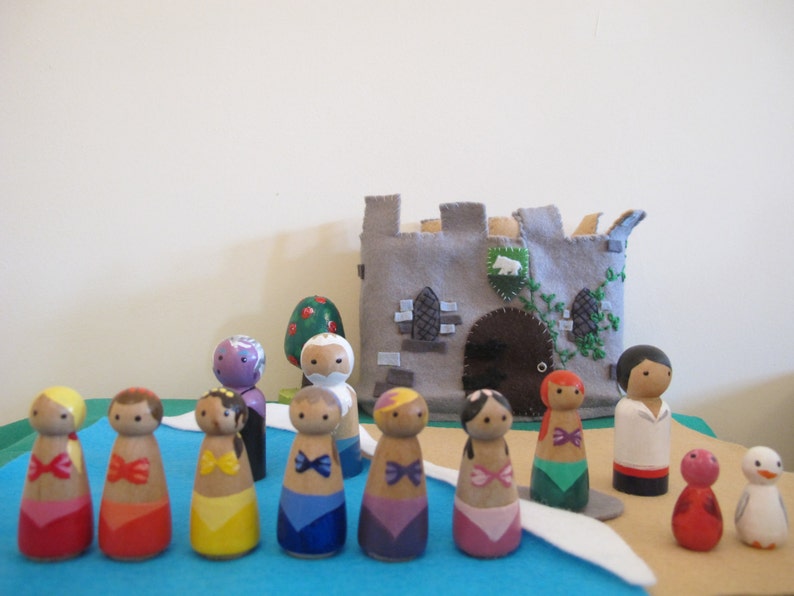 May include: A set of wooden dolls with painted faces and colorful clothing, including a castle, a tree, and a bird. The dolls are arranged in a line on a blue surface.
