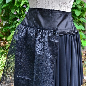 May include: A black skirt with a lace overlay. The skirt is asymmetrical and has a high waist. The lace overlay is sheer and has a floral pattern.