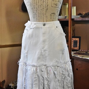 May include: A white denim skirt with a lace trim and frayed edges. The skirt is on a mannequin and has a vintage feel.