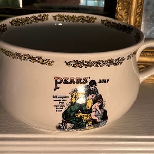 Pode incluir: Tigela de cerâmica branca com um design floral dourado em torno da borda. A tigela apresenta um anúncio vintage de sabonete Pears' com uma mulher e uma criança a tomar banho. O texto diz "Vendido em todos os lugares, tabletes insuperáveis 6d cada, tabletes maiores perfumados 1/- cada."