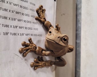 May include: A brown frog figurine with articulated limbs is perched on a white sheet of paper with a list of air fitting sizes. The list includes sizes for straight and 90-degree fittings, with different tube and MPT sizes.
