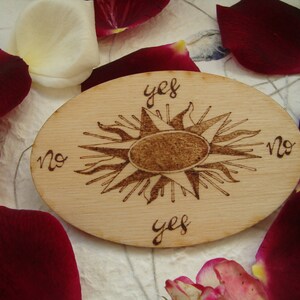 Può includere: Un tagliere di legno con un disegno di sole e le parole "sì" e "no" scritte intorno. Il tagliere è circondato da petali di rosa.
