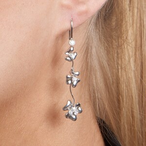 May include: Silver dangle earrings with a cluster of three flower-shaped charms.