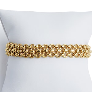 May include: A gold chain bracelet with a delicate, intricate design. The bracelet is displayed on a white pillow.