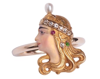 May include: A gold ring with a detailed portrait of a woman's face. The woman is wearing a crown with diamonds and a pearl. The ring is set with rubies and emeralds.