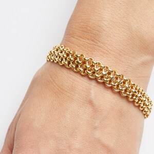 May include: A gold chain bracelet with a unique, interwoven design. The bracelet is made of multiple rows of linked gold circles.