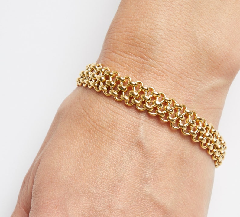 May include: A gold chain bracelet with a unique, interwoven design. The bracelet is made of multiple rows of linked gold circles.