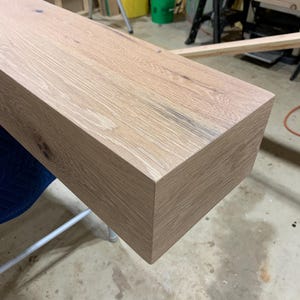 May include: A close-up of a light-colored wooden shelf with a smooth, slightly textured surface. The shelf has a rectangular shape with rounded edges and is made of natural wood.