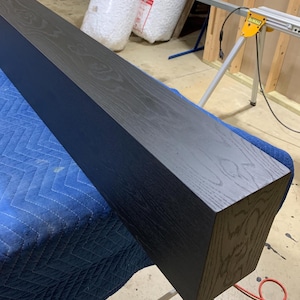 May include: A long, dark stained wooden beam with a rectangular cross-section. The beam is resting on a blue tarp.