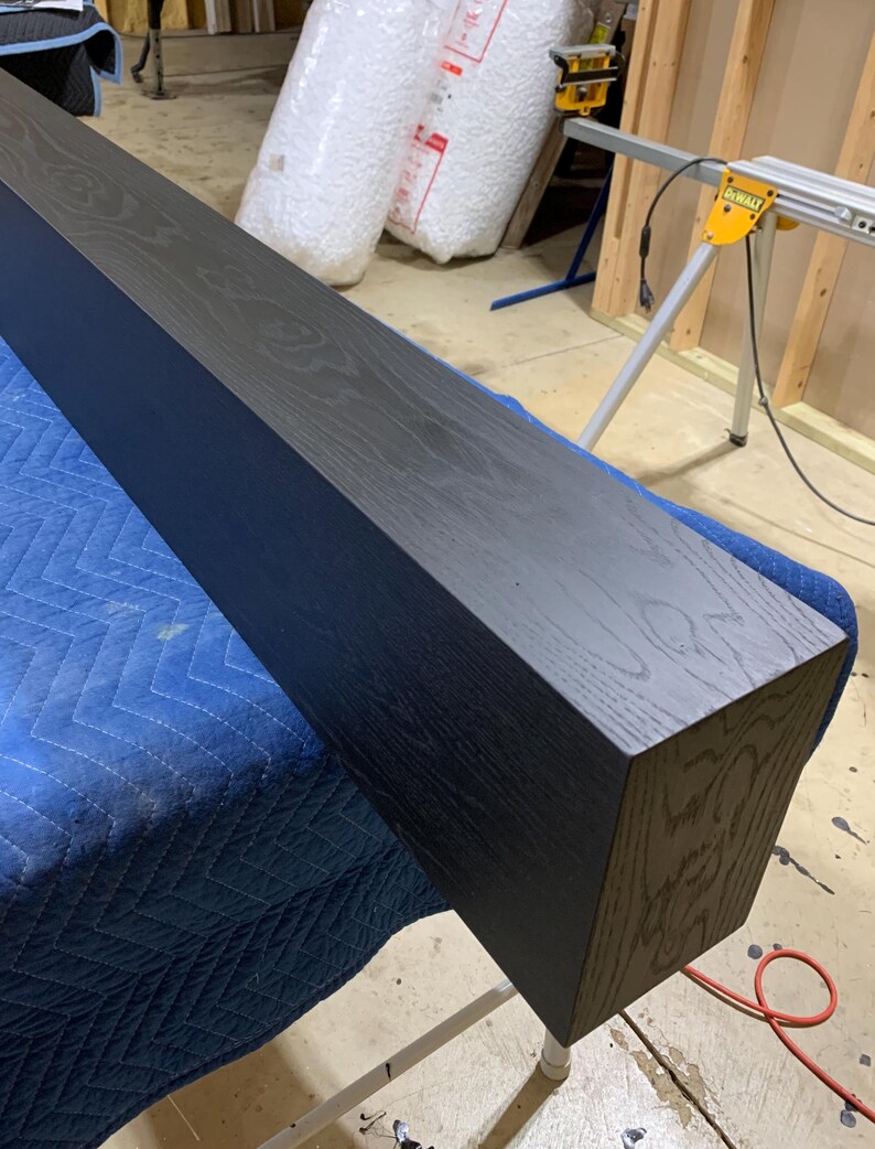 May include: A long, dark stained wooden beam with a rectangular cross-section. The beam is resting on a blue tarp.