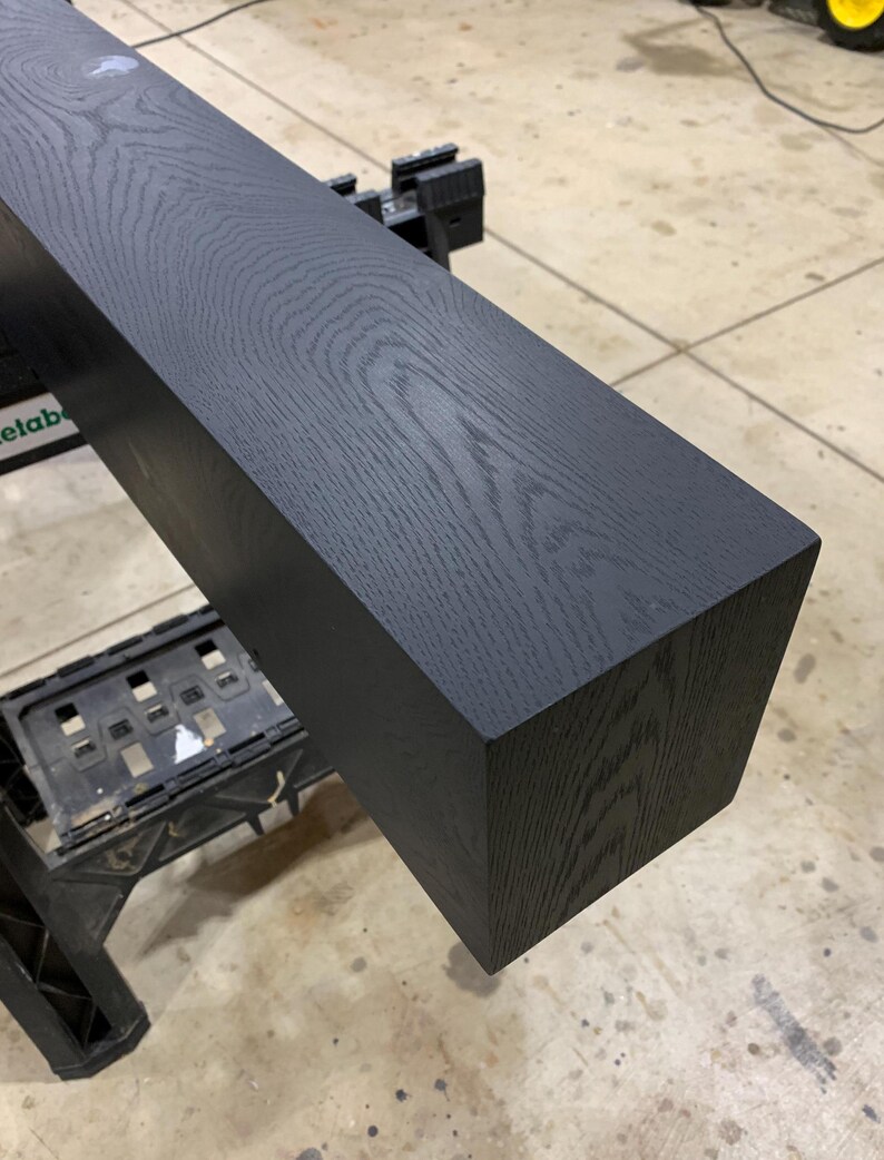 May include: A black stained wooden beam with a square cross-section. The wood grain is visible in the dark stain.