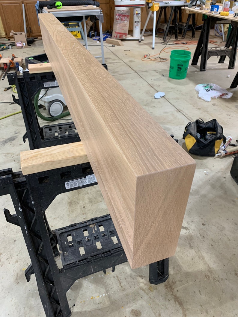 May include: A long, light brown wooden beam resting on two black sawhorses. The beam has a smooth, polished surface and is likely made of oak.