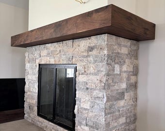 May include: A fireplace with a stone facade and a dark wood mantel. The stone is a mix of gray and beige tones. The fireplace has a black glass door. The mantel is a dark brown, rectangular shape.