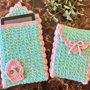 May include: Two crocheted phone cases in a teal and pink color scheme. The larger case has a skull design and the smaller case has a bow design.