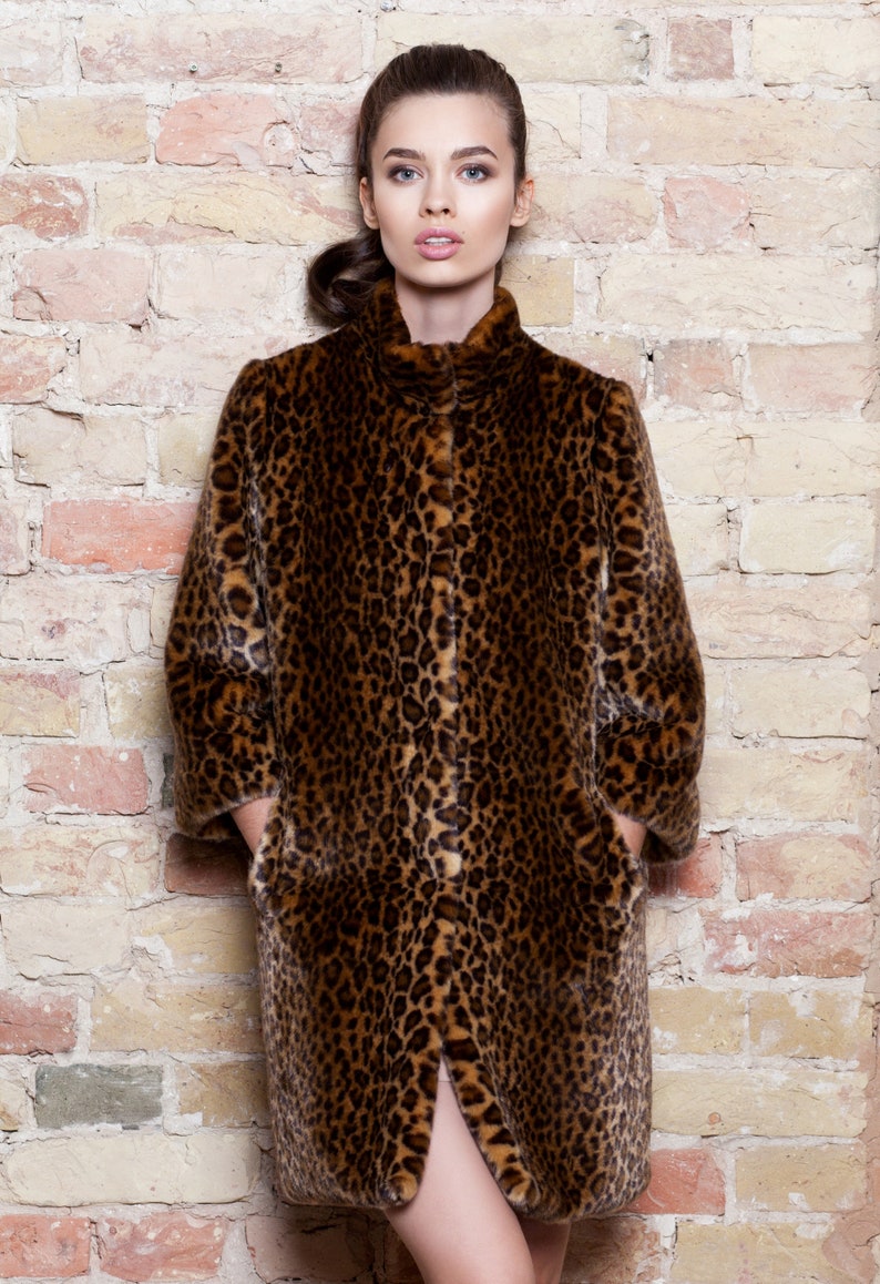 Pu&ograve; includere: Un cappotto lungo con stampa leopardata, colletto alto e tasche. Il cappotto presenta un motivo maculato marrone e nero. La modella &egrave; in piedi davanti a un muro di mattoni. Il cappotto &egrave; lungo fino al ginocchio.