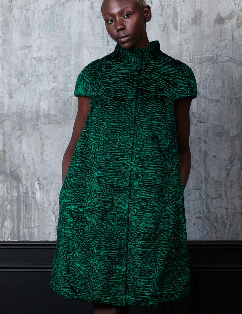 May include: A short-sleeved, knee-length dress in a vibrant emerald green. The dress features a high, rounded collar and a textured, patterned fabric. The garment is buttoned down the front and has a tailored fit.